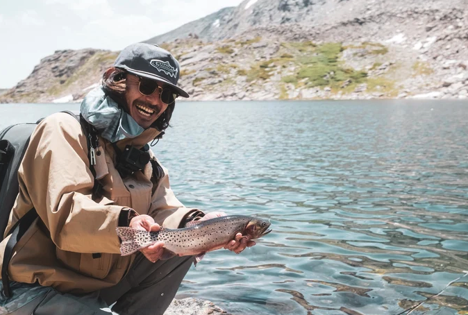 Angler holding fish while wearing Yakoda Trout Logo Hat Steel color