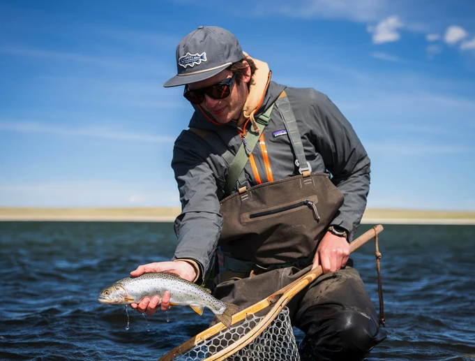 Angler holding fish while wearing Yakoda Trout Logo Hat Steel color and holding net